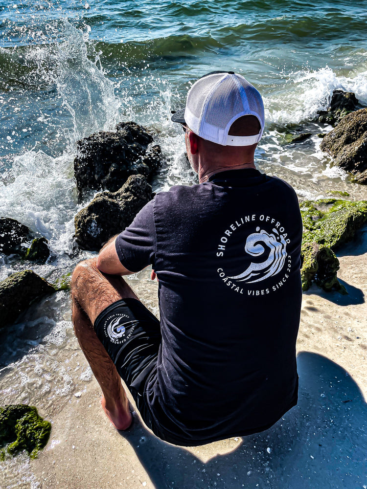 Rear view of a shoreline Offroad shirt and shorts next to the rocks and ocean.