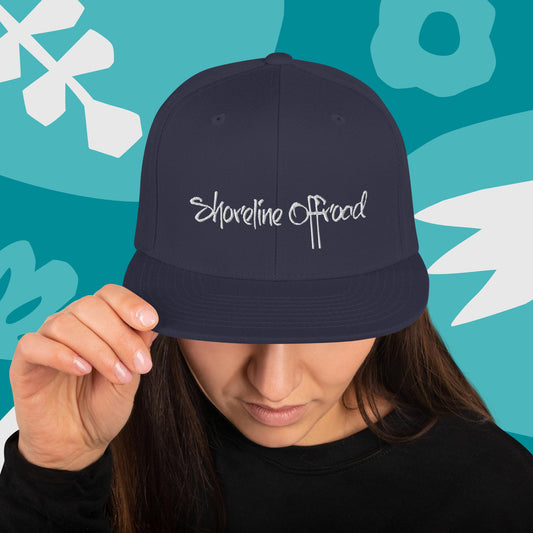 a woman holding a hat with the word shoreline road on it