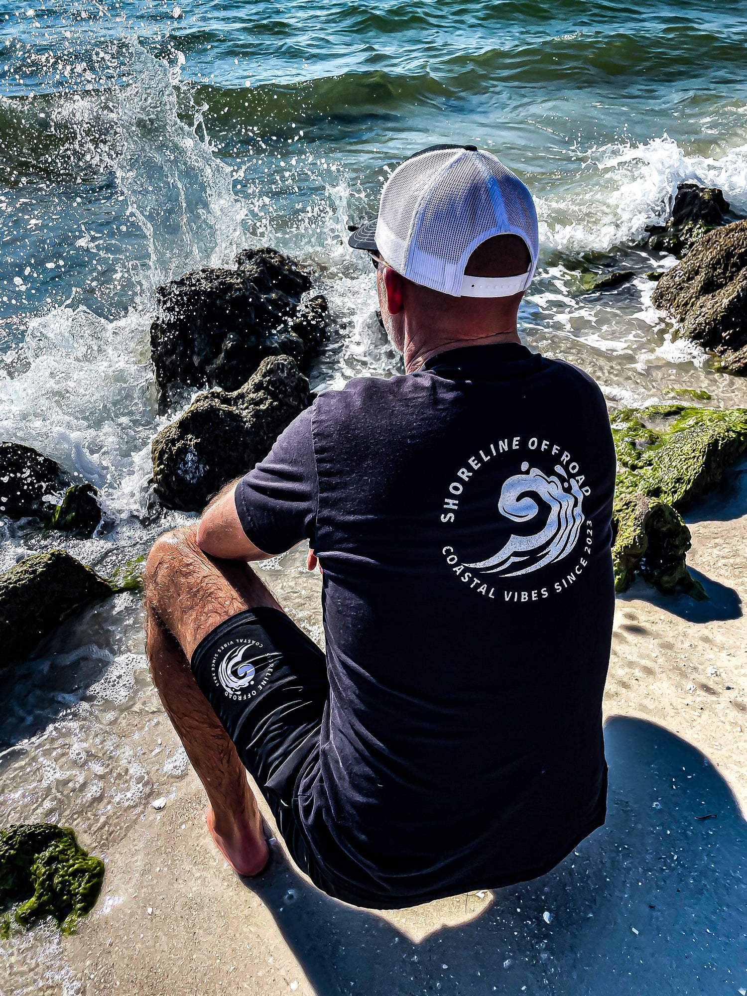 Rear view of a shoreline Offroad shirt and shorts next to the rocks and ocean. 