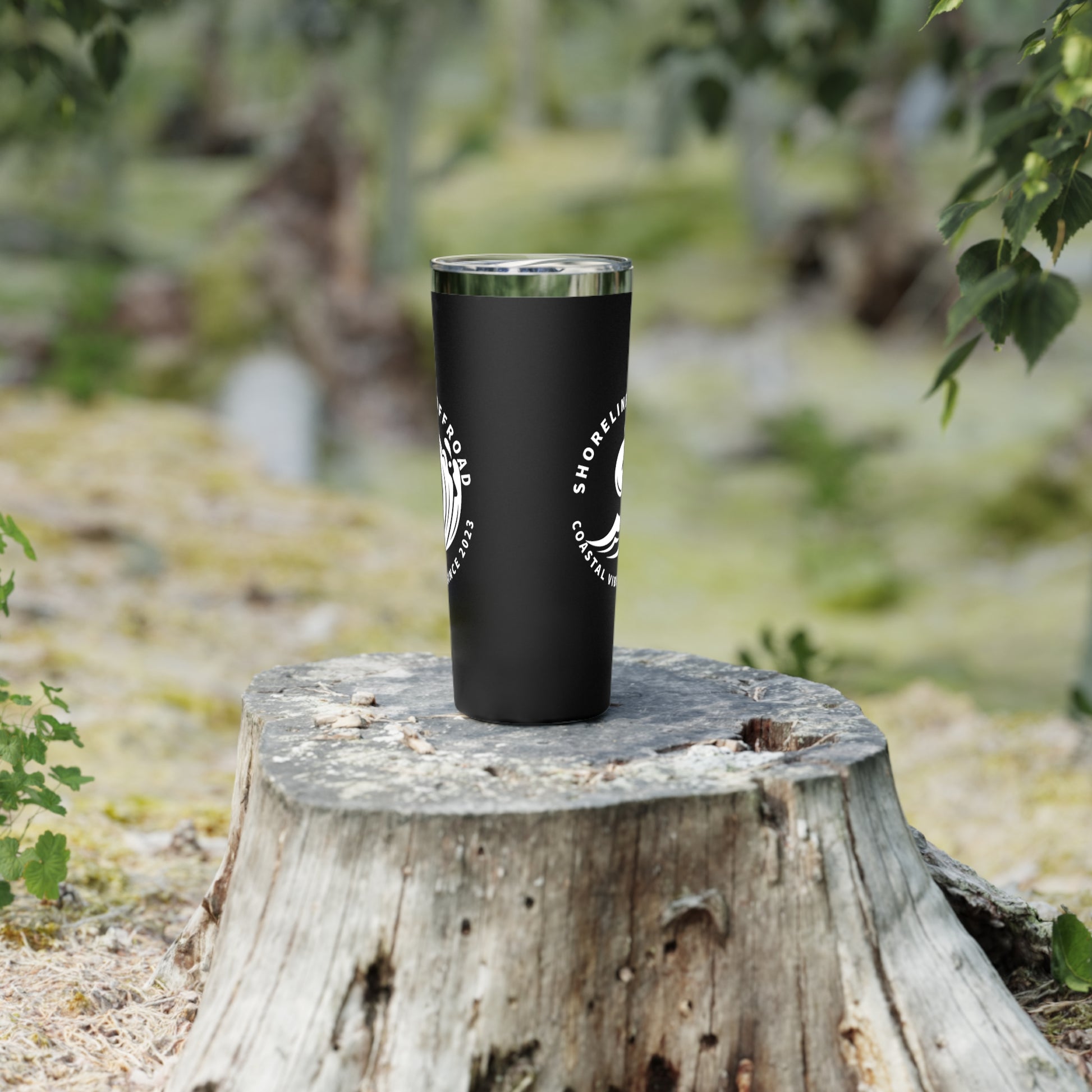 a black tumbler cup sitting on top of a tree stump