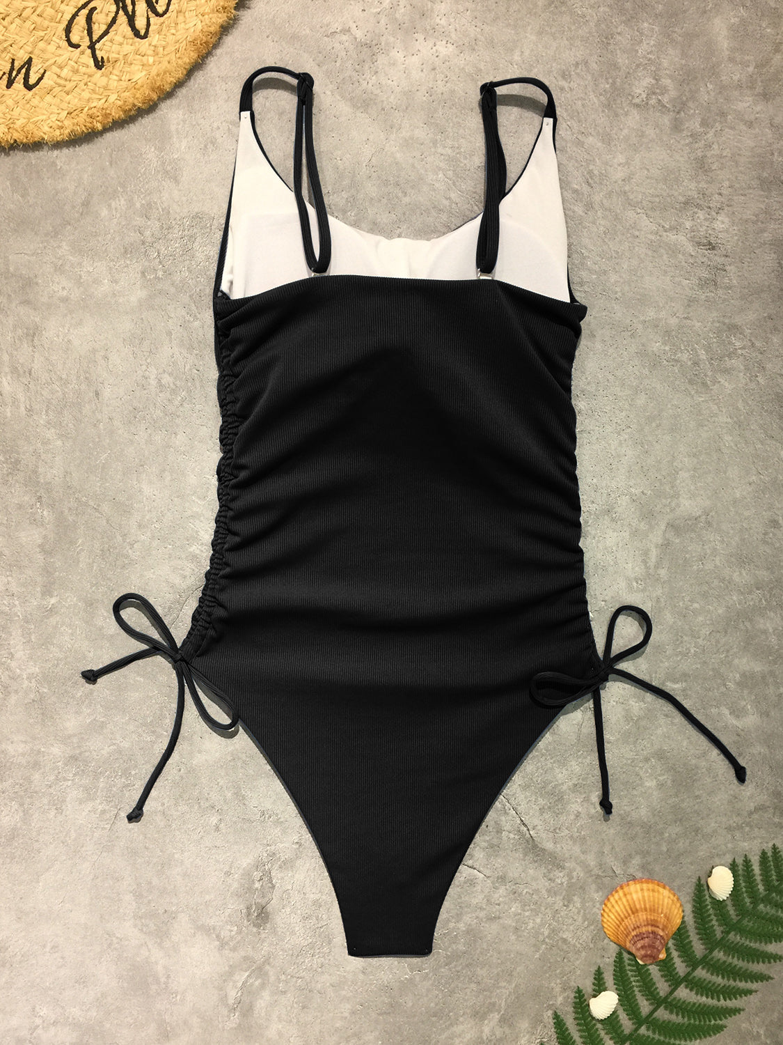 a black and white one piece swimsuit next to a plant