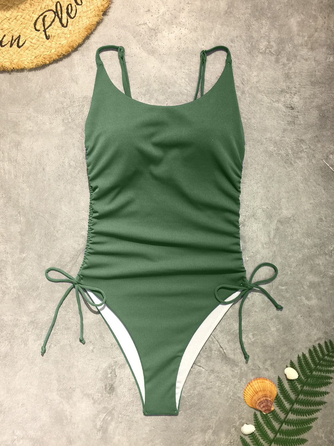 a green and white one piece swimsuit next to a plant