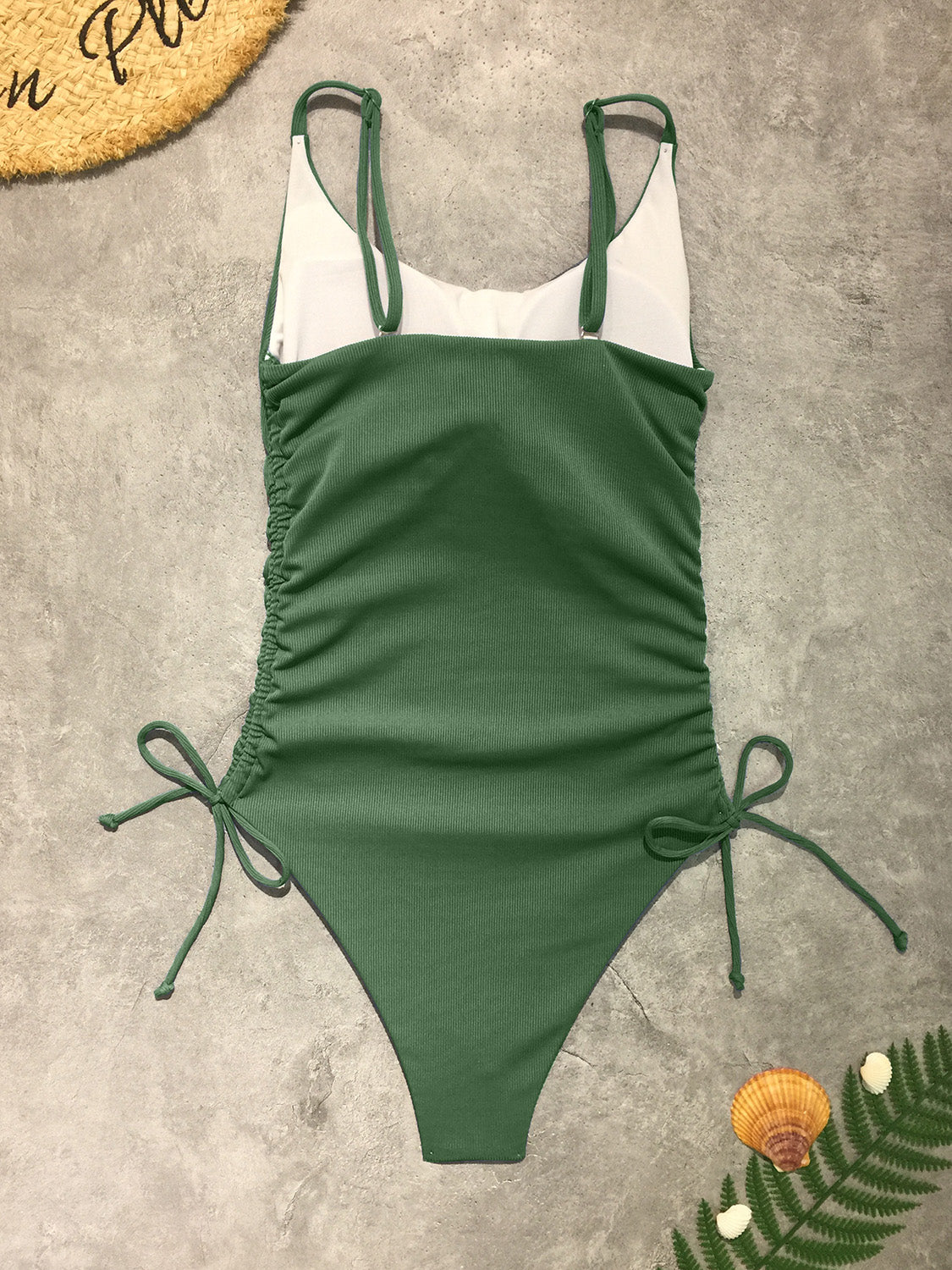 a green and white one piece swimsuit next to a plant