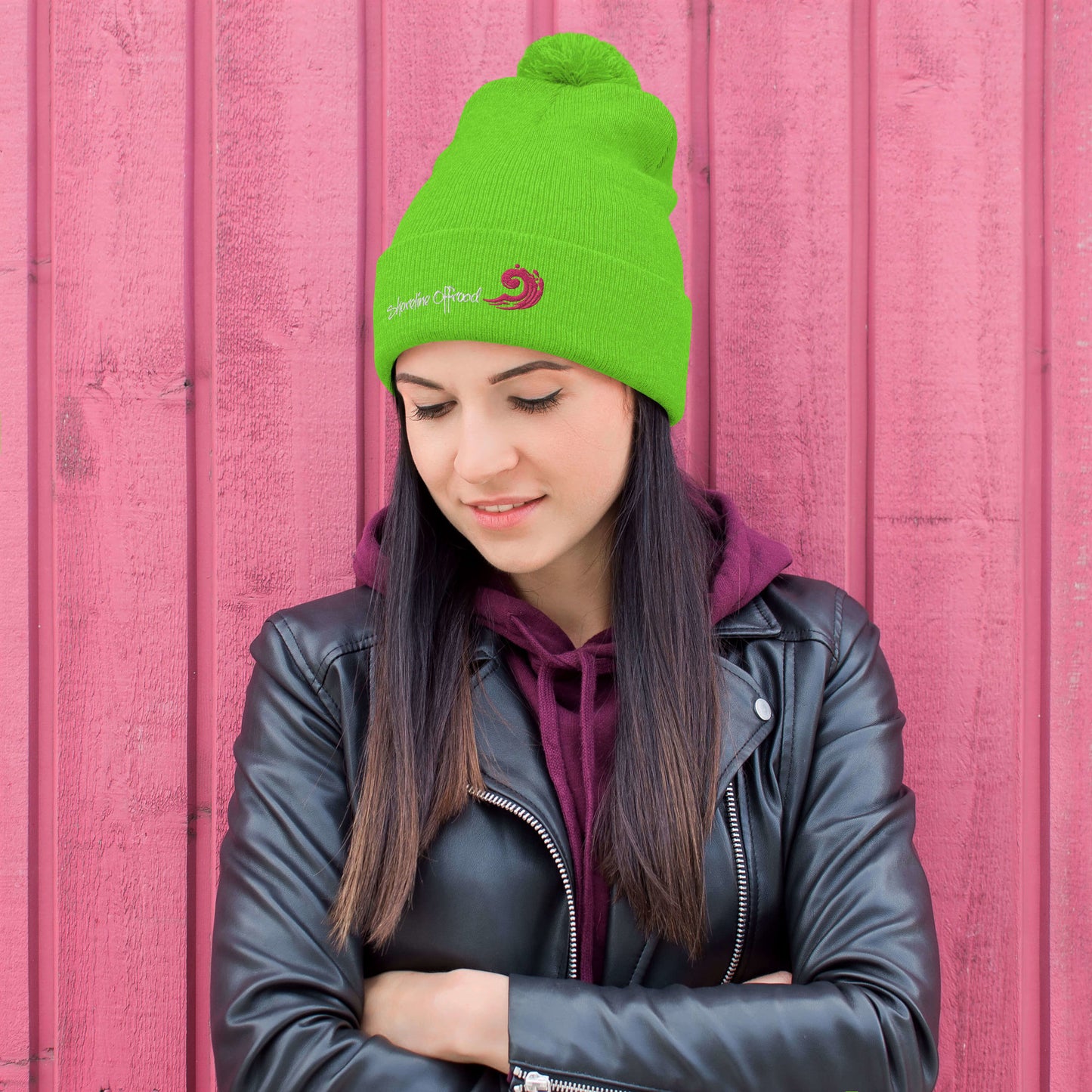 a woman wearing a green beanie standing in front of a pink wall