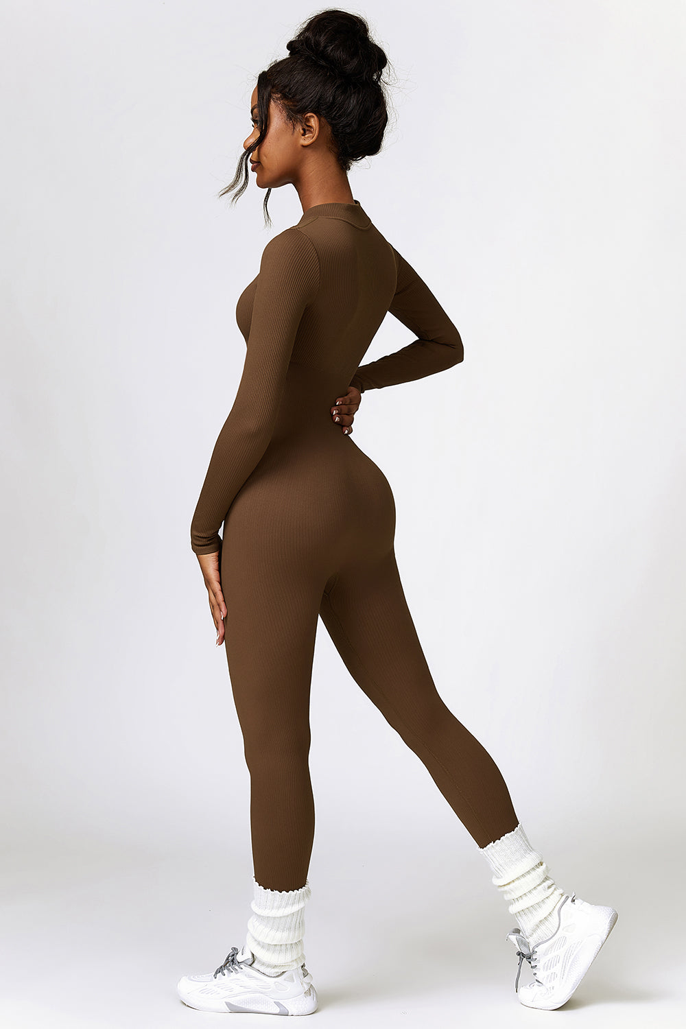 a woman wearing a brown bodysuit and white sneakers