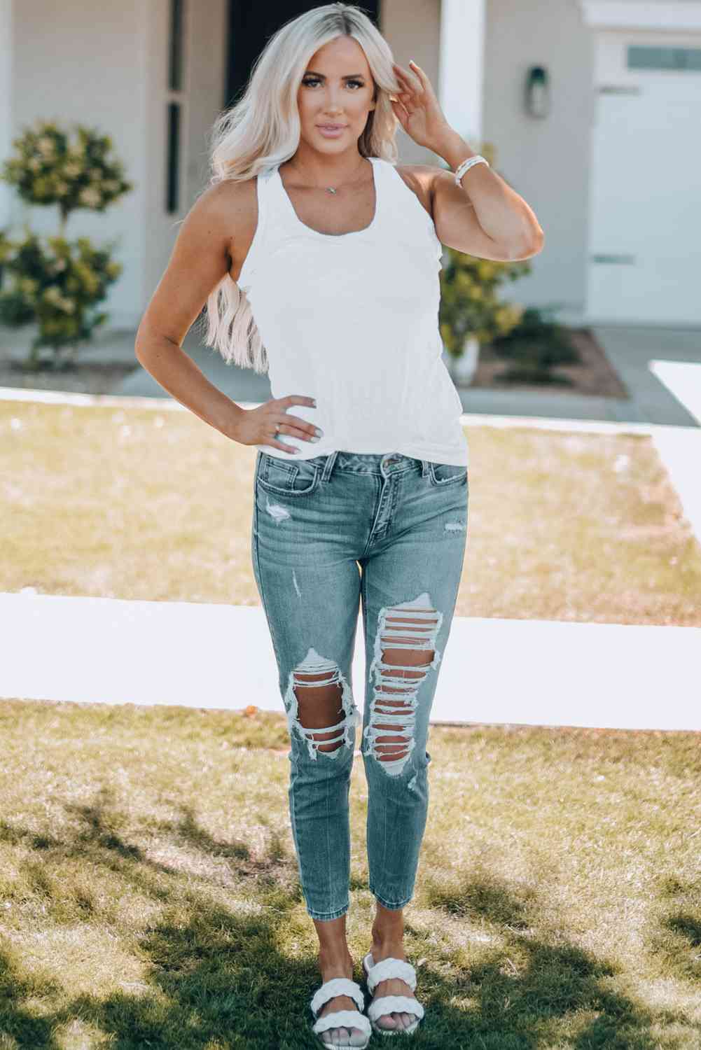 a woman wearing ripped jeans and a white tank top